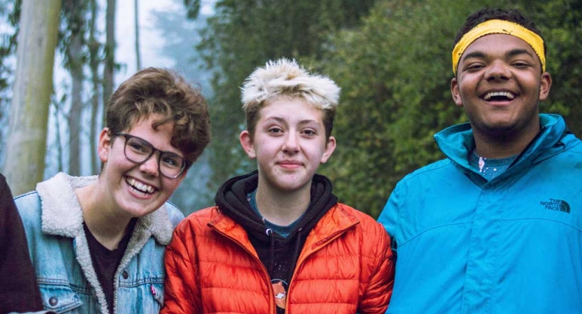 Three students smile for the photo in a wooded area. 